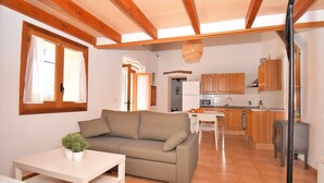 A compact living space with a sofa, a dining table, and a kitchen area including a refrigerator, microwave, and wooden cabinets. - Es Camp Pla 087 cosy finca with private pool, terrace, garden, barbecue and air-conditioning (Sineu)