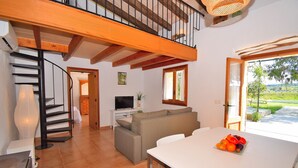 A spacious living area with a staircase, a sofa, a dining table with fruit, and a television. - Es Camp Pla 087 cosy finca with private pool, terrace, garden, barbecue and air-conditioning (Sineu)