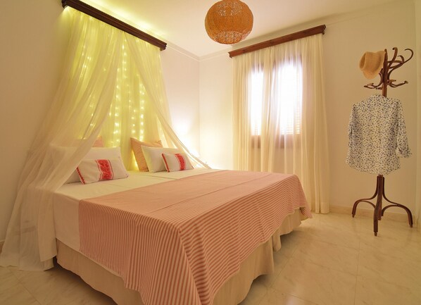 A neatly made bed with a striped bedspread, a canopy with lights, and a coat stand with a hat.