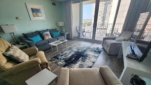 Una sala de estar moderna con sofá, sillón y una mesita de centro. Hay un balcón con vistas a la ciudad.