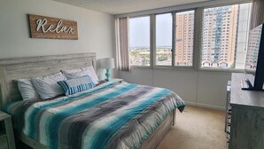 Un dormitorio con una cama grande, una mesita de noche, un aparador y una ventana con vista a la ciudad.
