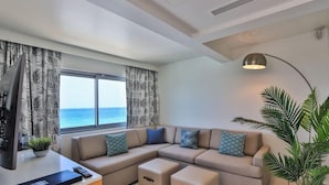 A modern living room with a sectional sofa, ottomans, a flat-screen TV, and a large window with a view of the sea. - The Morgan Resort & Spa (Simpson Bay)