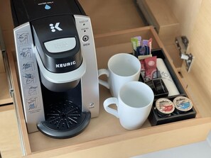 A Keurig coffee maker in a drawer with two white mugs and coffee pods.