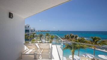 A balcony with a clear view of the ocean, lounge chairs, and a pool area.