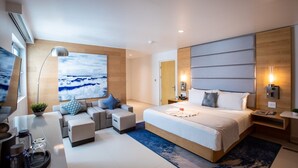 A modern hotel room with a large bed, a seating area with sofas, a large painting, and a view of the sea. - The Morgan Resort & Spa (Simpson Bay)