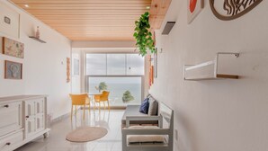 A modern living room with a wooden ceiling, a dining area with yellow chairs, and a view of the ocean. - RV03 Quarto e Sala Vista Mar (Salvador)