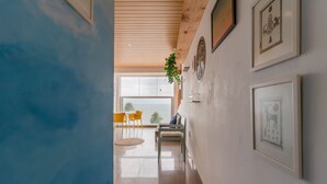 A hallway with a wooden ceiling, a plant, and framed artwork on the walls. - RV03 Quarto e Sala Vista Mar (Salvador)