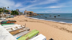 A beach with boats, a building, and a clear sky. - RV03 Quarto e Sala Vista Mar (Salvador)