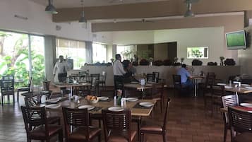 Un comedor amplio con varias mesas y sillas, ventiladores de techo y ventanas grandes que permiten la entrada de luz natural.