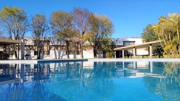 Piscina com superfície de água azul límpida, cercada por árvores e edifícios modernos.