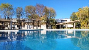 A swimming pool with a clear blue water surface, surrounded by trees and modern buildings. - Hotel Villablanca (Tehuacán)