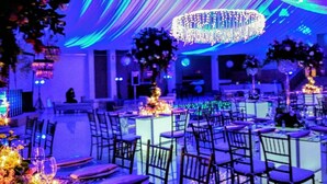 Salão de banquetes com mesas montadas para um evento formal, apresentando um lustre grande e teto decorado com tecidos.