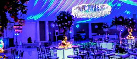 A banquet hall with tables set for a formal event, featuring a large chandelier and draped ceiling.