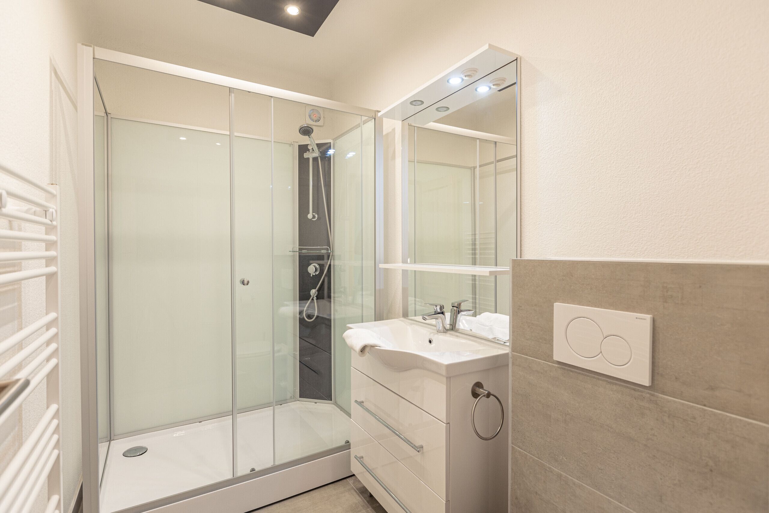 A modern bathroom with a glass-enclosed shower, a white sink, and a mirror above the vanity.