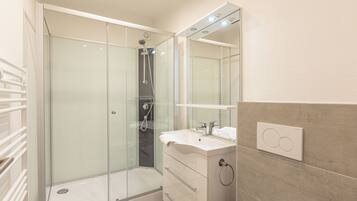 A modern bathroom with a glass-enclosed shower, a white sink, and a mirror above the vanity.
