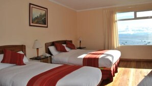 Une chambre d’hôtel avec deux lits, un tableau au mur et une fenêtre donnant sur la mer.