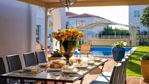 A dining table set for breakfast with a vase of flowers, a pool, and a covered patio area. - Villa Palazzo di Zara with Pool (Vabriga)