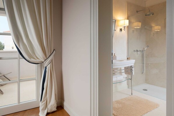 A modern bathroom with a glass shower enclosure, a white sink, and a beige rug.
