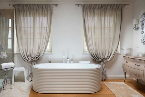 Ein modernes Badezimmer mit freistehender Badewanne, einem Waschtisch mit Spiegel und zwei mit Vorhängen versehenen Fenstern.