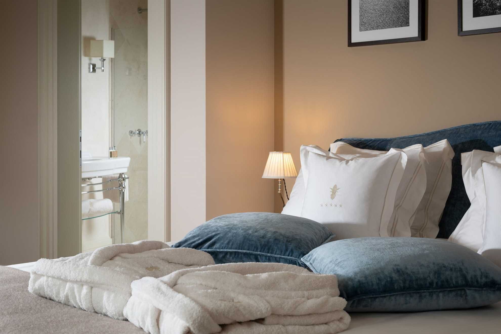 Ein Hotelzimmer mit einem Bett, einer Nachttischlampe, einem Spiegel und einem durch eine offene Tür einsehbarer Badezimmer.