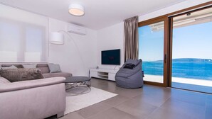 A modern living room with a sofa, a coffee table, a bean bag, a TV, and a view of the sea through a sliding glass door. - Beachfront Villa Sea Touch (Okrug Donji)