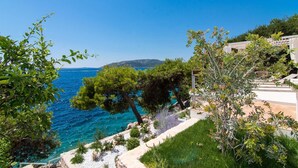 A coastal view with a clear blue sea, a grassy area, and a white building with a balcony overlooking the sea. - Beachfront Villa Sea Touch (Okrug Donji)