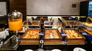 Buffet com diversas opções de comida, incluindo suco de laranja, pão e doces.