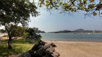 A beach with a rocky foreground, a clear view of the sea, and boats in the distance.