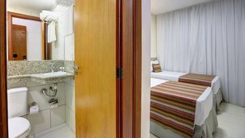 A hotel room with a bathroom, a bed with a striped blanket, and a curtain.
