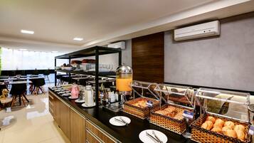 Buffet de café da manhã com diversos alimentos e um dispensador de suco.