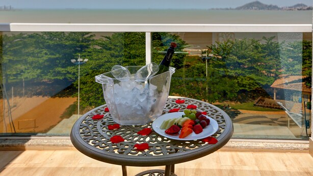 A table with a bottle of champagne, ice, and a plate of fruit on a balcony overlooking a scenic view.