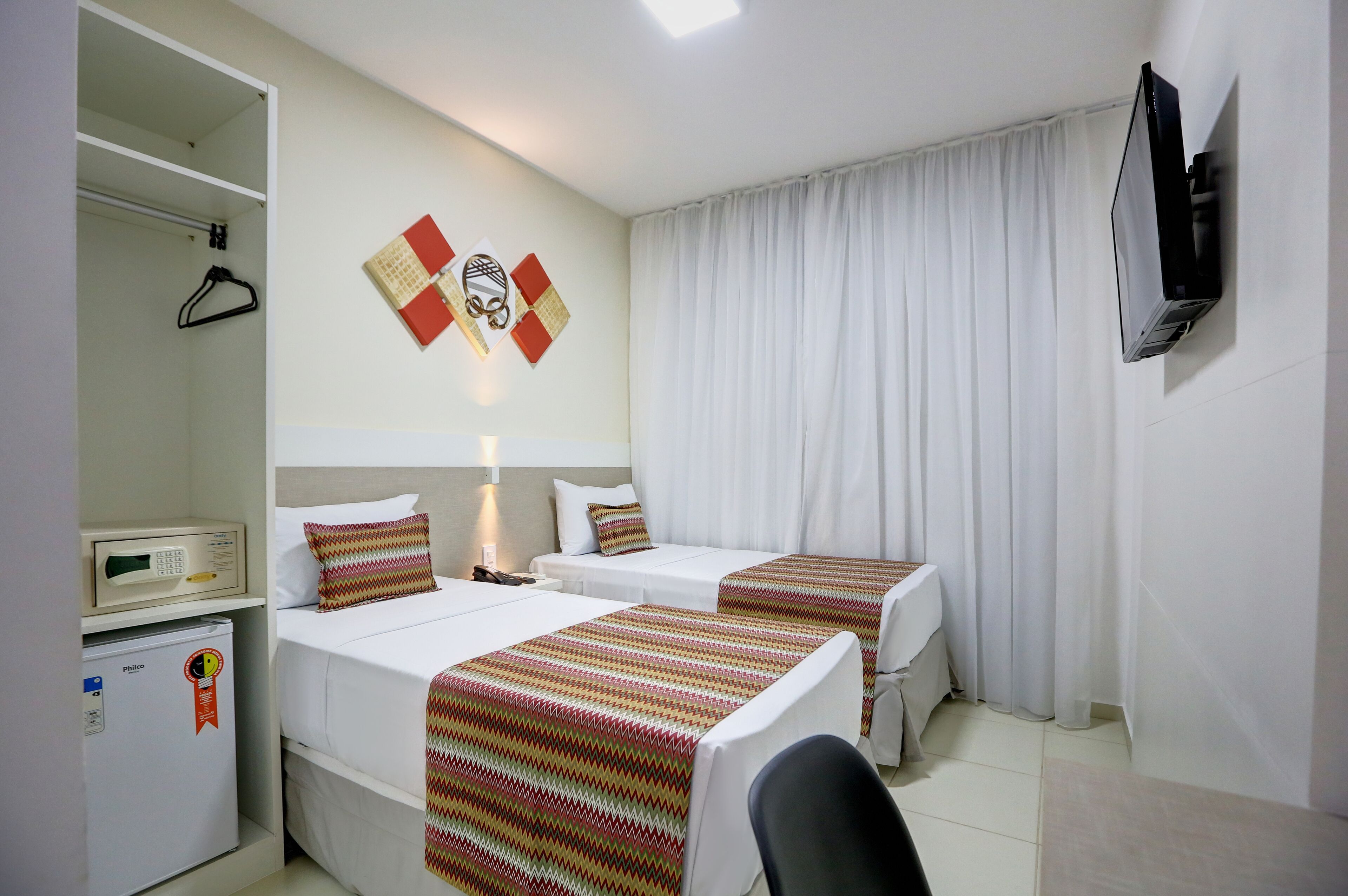 Habitación de hotel con dos camas, un televisor montado en la pared, un minibar y un perchero.
