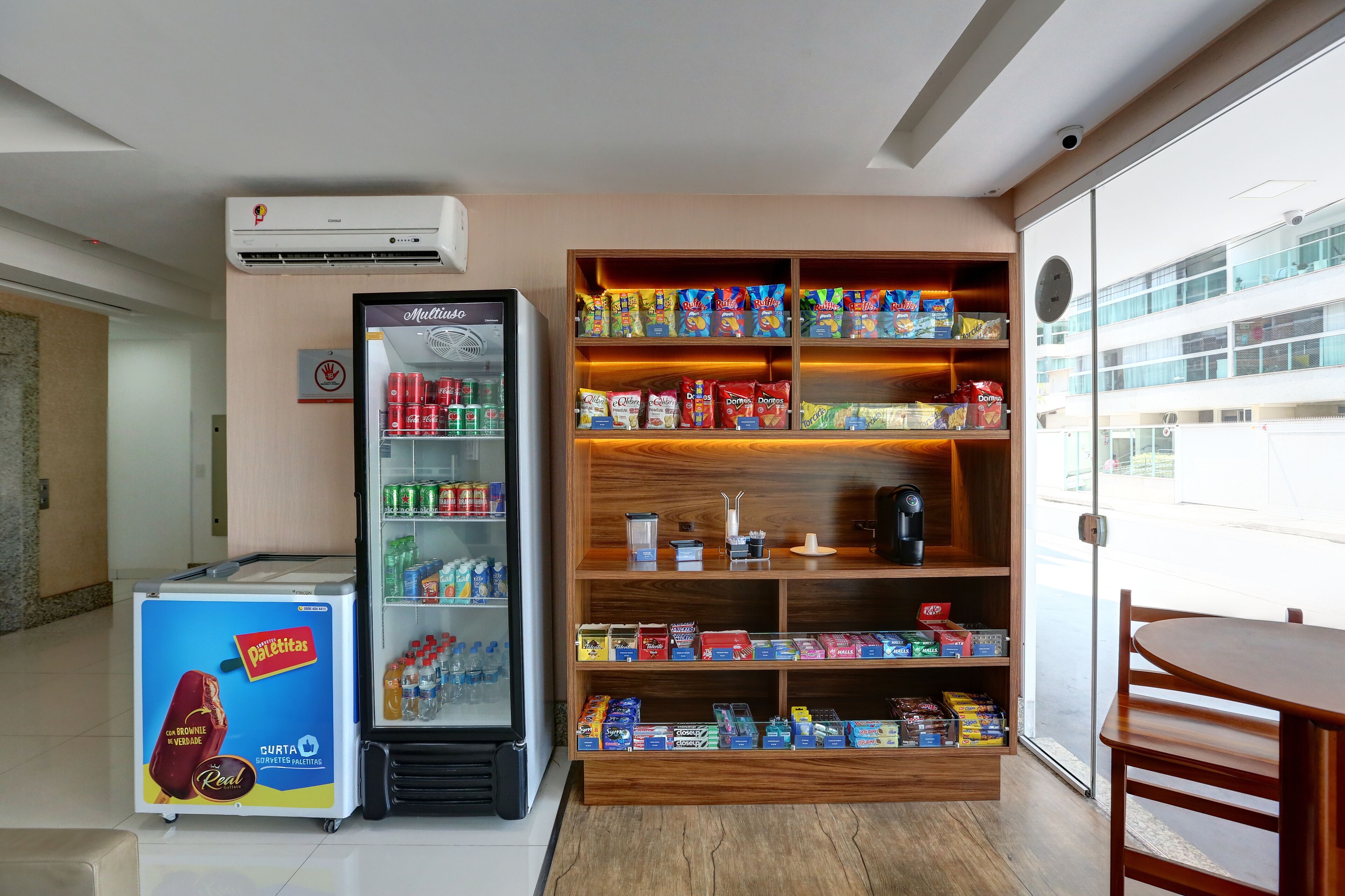 Una habitación con un refrigerador lleno de bebidas, una máquina expendedora y una repisa con aperitivos y artículos de aseo.