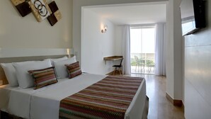 A hotel room with a bed, a desk, a chair, a TV, and a balcony with curtains.