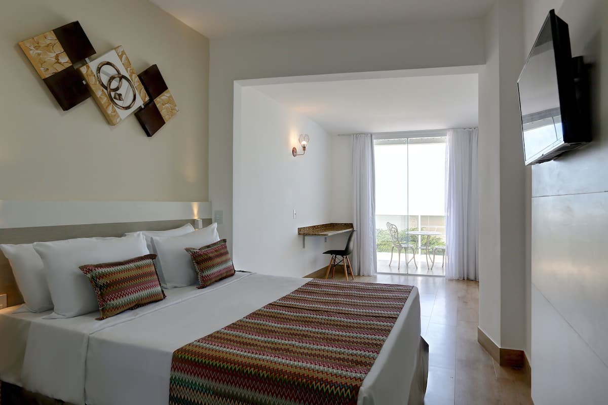 A hotel room with a bed, a desk, a chair, a TV, and a balcony with curtains.