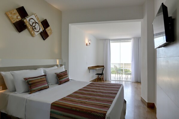 A hotel room with a bed, a desk, a chair, a TV, and a balcony with curtains. - Transamerica Fit Vitória Praia de Camburi (Vitoria)