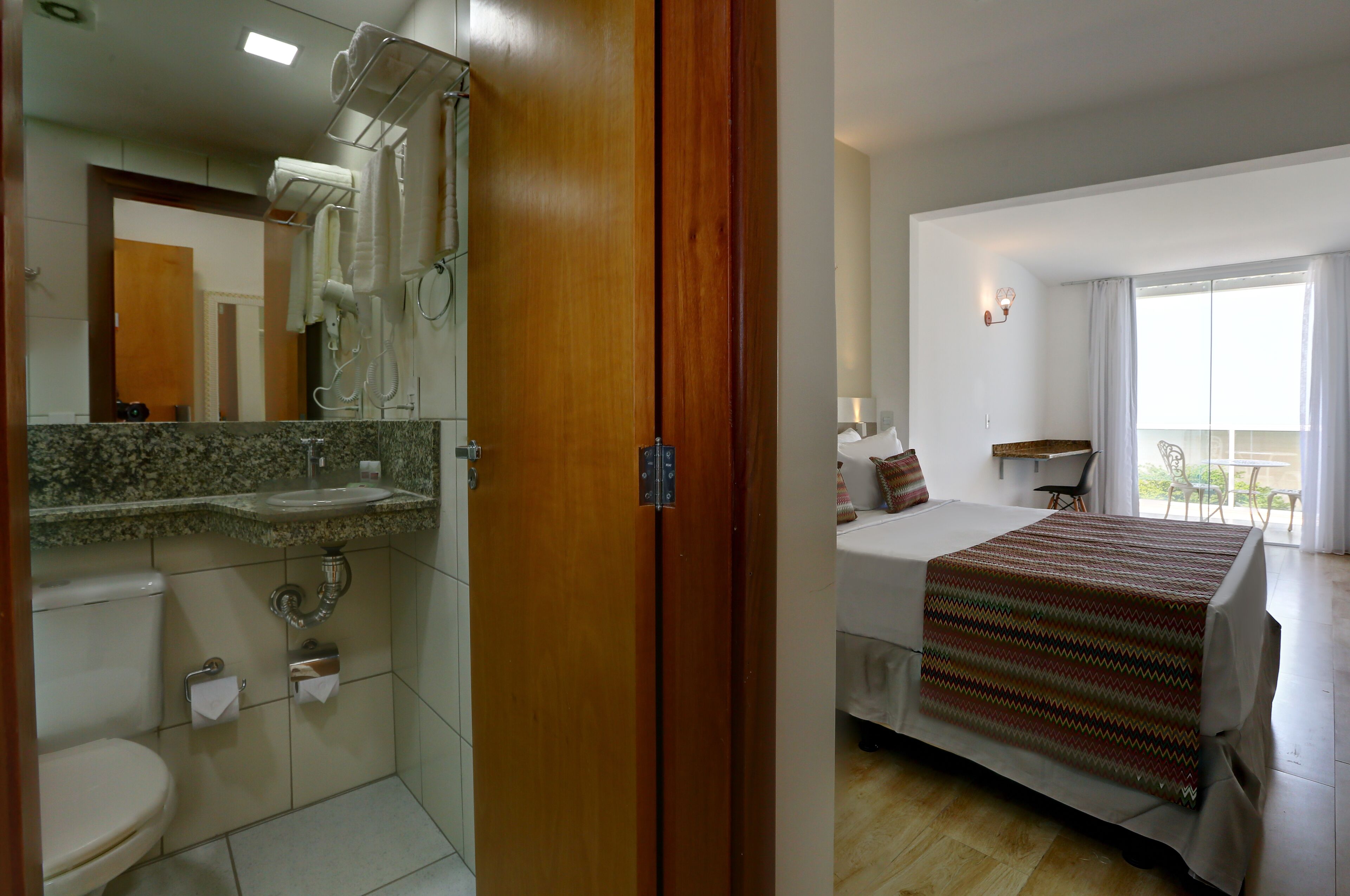 Habitación de hotel con baño, cama, ventana y balcón.