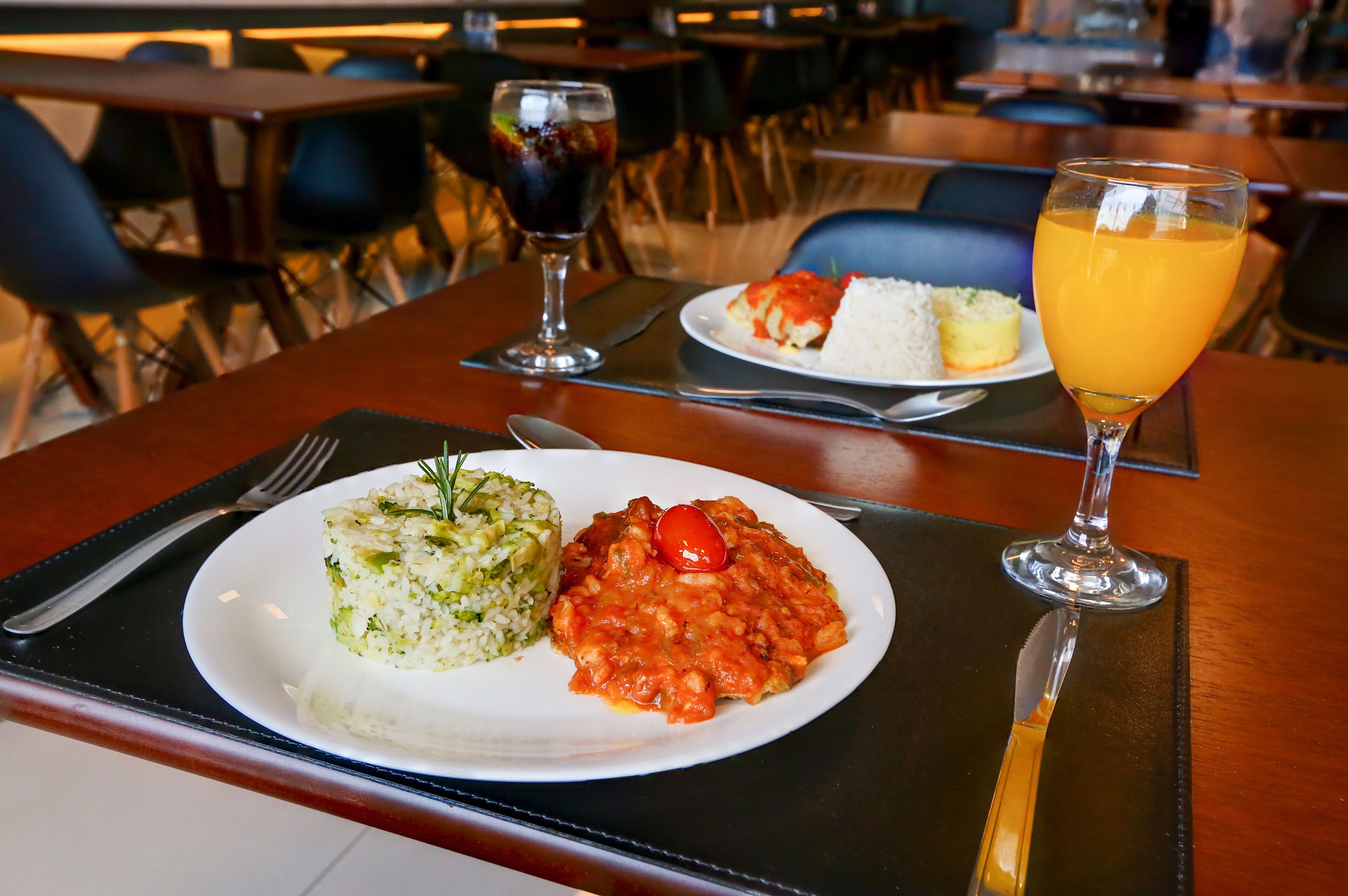 Una mesa de comedor con un plato de comida, un vaso de zumo de naranja y un tenedor.