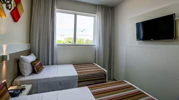 Habitación de hotel con dos camas, televisión, ventana con cortinas y vista a zonas verdes.