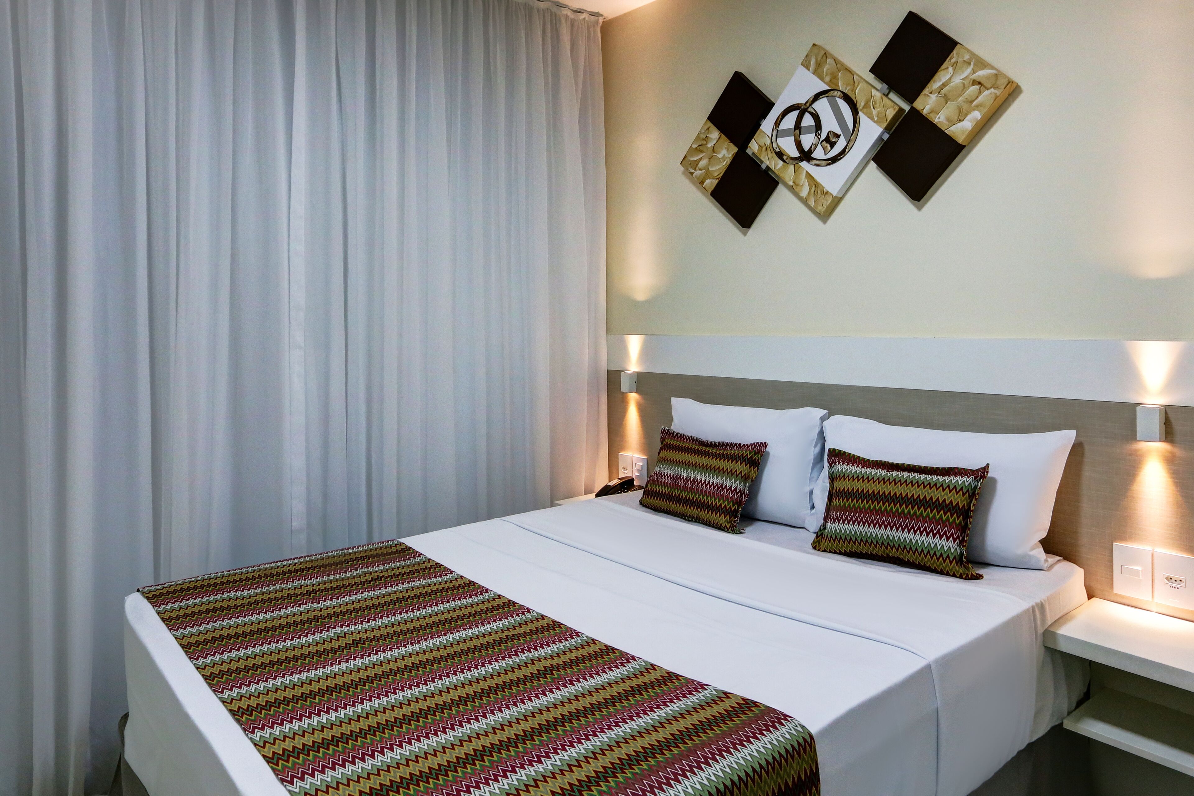 Een hotelkamer met een opgemaakt bed, een nachtkastje met een lamp en een aan de muur hangend kunstwerk.