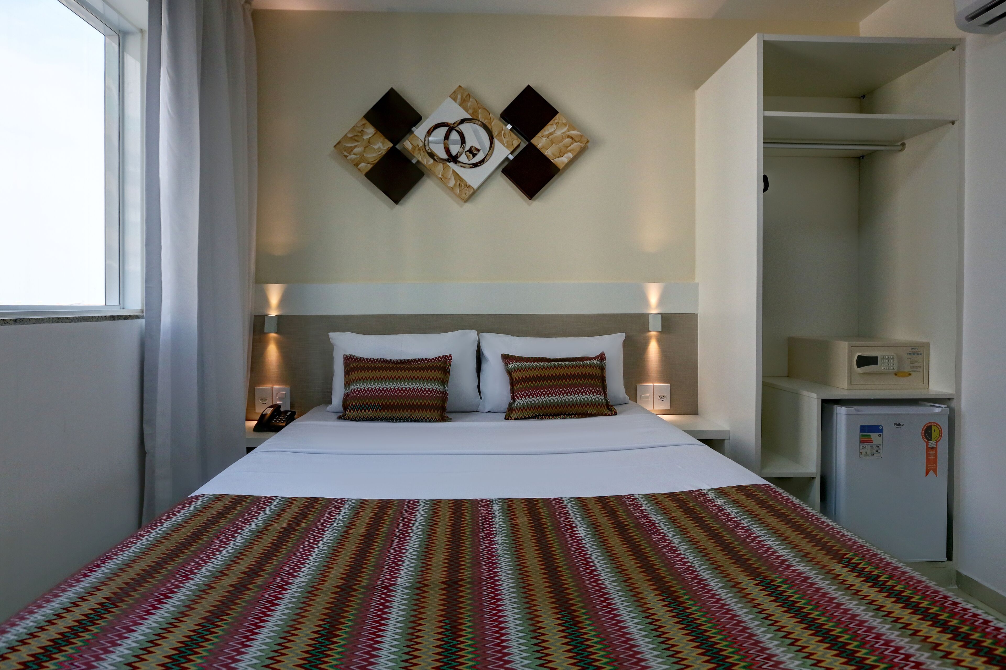 Habitación de hotel con cama, un refrigerador pequeño y una obra de arte colgada en la pared.