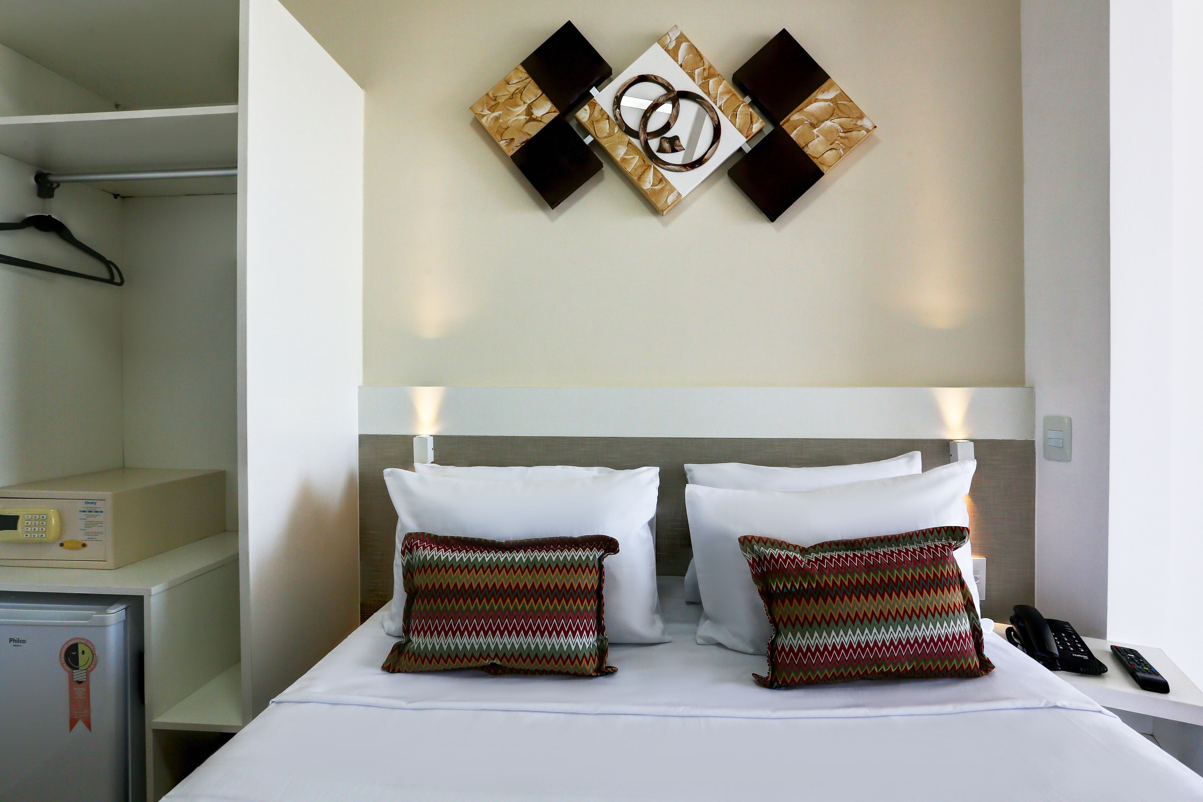 Habitación de hotel con cama, almohadas, mesita de noche con teléfono, microondas y perchero.