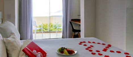 A hotel room with a bed, a plate of fruit, and rose petals arranged on the bed.