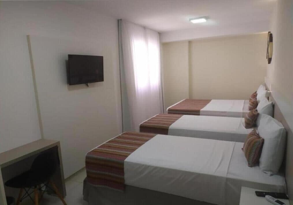 A hotel room with two beds, a TV mounted on the wall, and a desk with a chair.