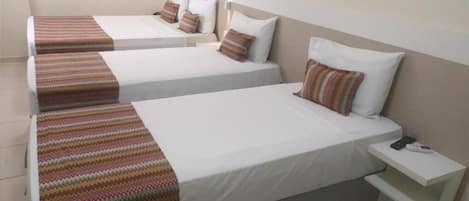 A hotel room with two beds, each with a striped blanket and pillows, a bedside table with a phone, and a wall-mounted light fixture.