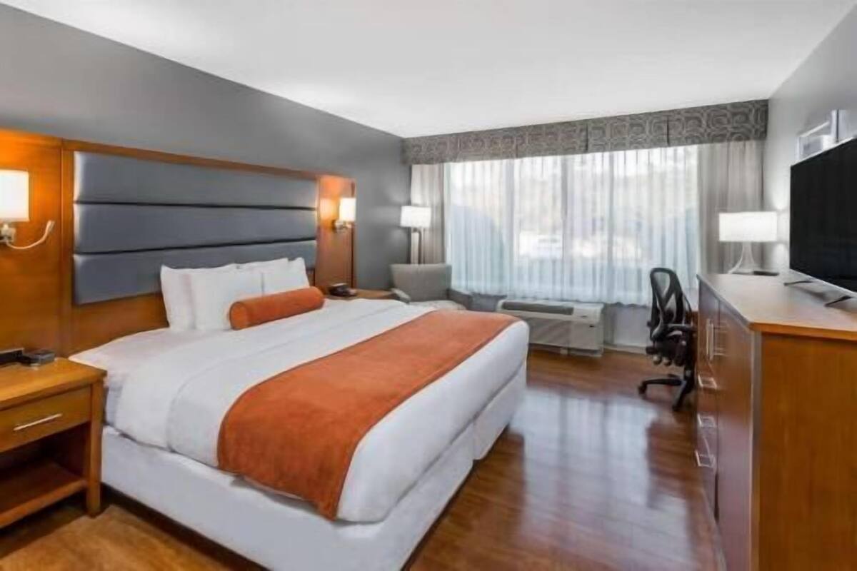 Une chambre d’hôtel équipée d’un lit, d’un bureau, d’une chaise, d’une télévision et d’une fenêtre avec des rideaux.