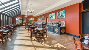 A spacious dining area with wooden tables and chairs, a bar counter, and large windows allowing natural light. - Wyndham Garden Greensboro (Greensboro)