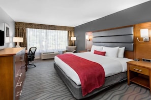 A hotel room with a large bed, a desk, a chair, a TV, and a window with curtains. - Wyndham Garden Greensboro (Greensboro)