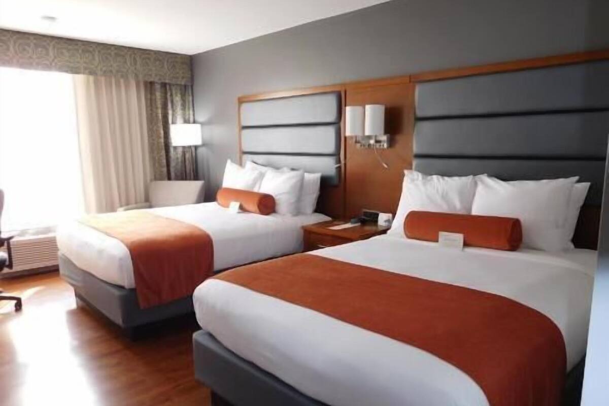Une chambre d’hôtel avec deux lits, une table de chevet, une lampe et une fenêtre avec des rideaux.