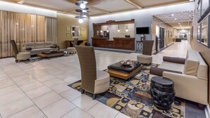 A spacious lobby with a sofa, armchairs, a coffee table, a patterned rug, a reception desk, and a TV. - Wyndham Garden Greensboro (Greensboro)